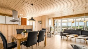 Eine moderne Küche mit Holzvertäfelung, einem Essbereich mit Tisch und Stühlen sowie einem Wohnbereich mit Sofa und Couchtisch.