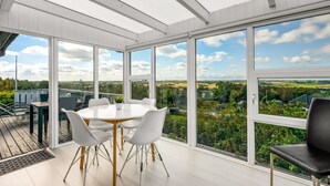 Ein moderner Wintergarten mit rundem Tisch und Stühlen, große Fenster mit Blick ins Grüne.