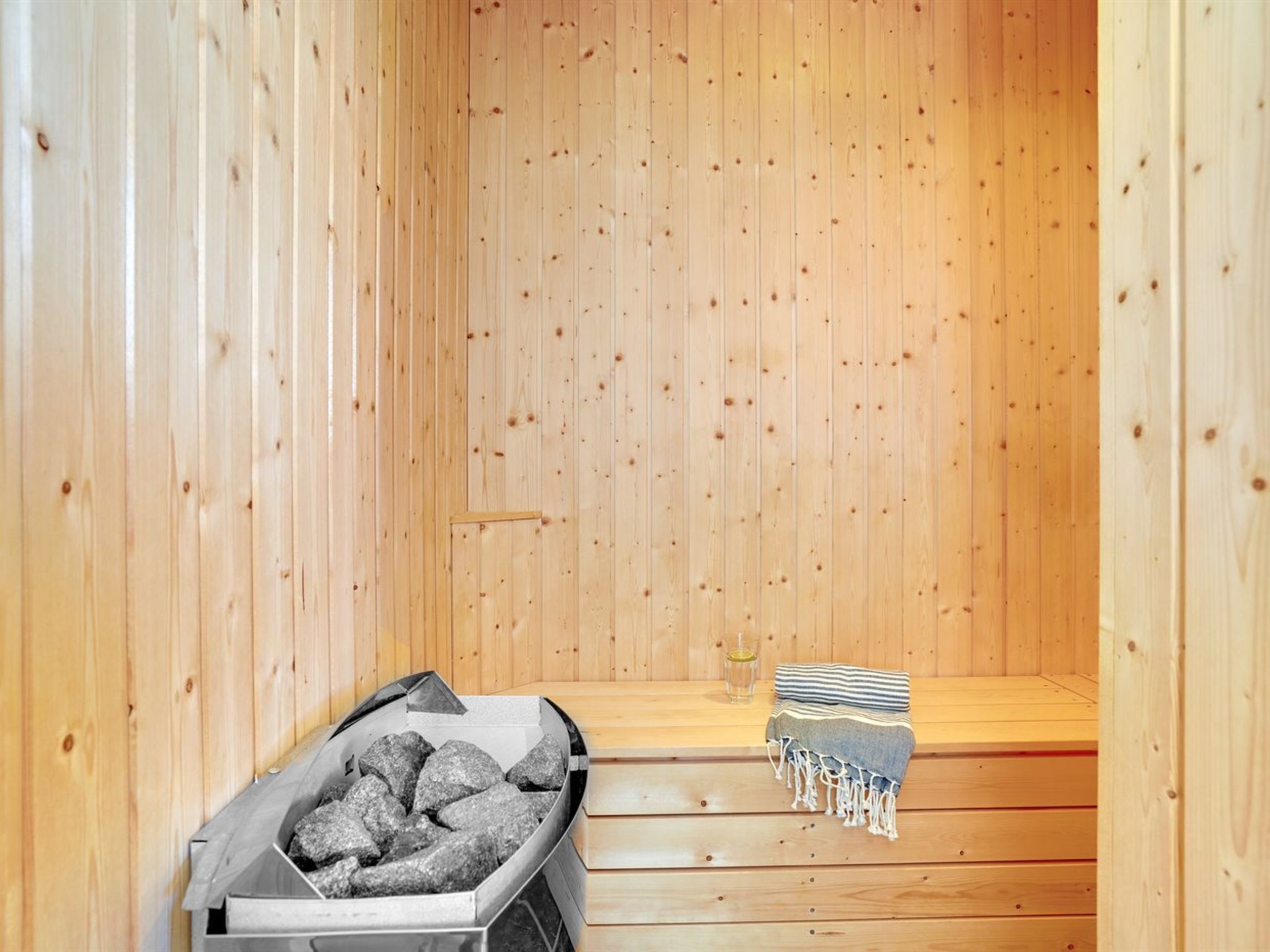 Un sauna avec des murs en bois, un banc, un récipient rempli de pierres et une serviette à rayures.