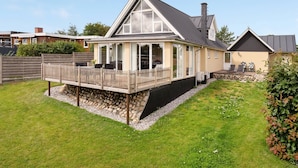 A modern house with a large deck, a stone foundation, and a well-maintained lawn.