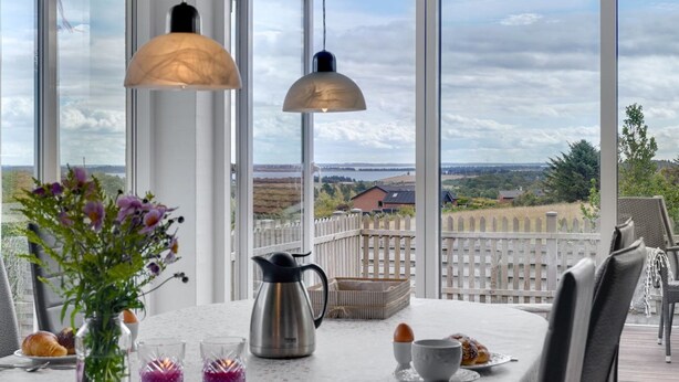 A dining area with a table set for two, a coffee pot, and a view of a wooden deck and landscape.