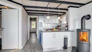 A modern kitchen with white cabinets, a central island, pendant lights, and a wood-burning stove.