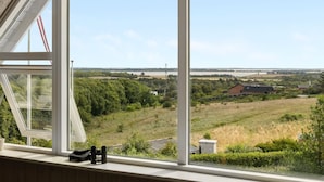 A room with a large window overlooking a rural landscape with fields and a distant bridge.