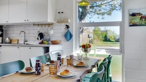 A kitchen with white cabinets, a wooden table set for dining, and a window with a view of a tree and a house. - "Tomine" - 500m to the fjord by Interhome (Struer)