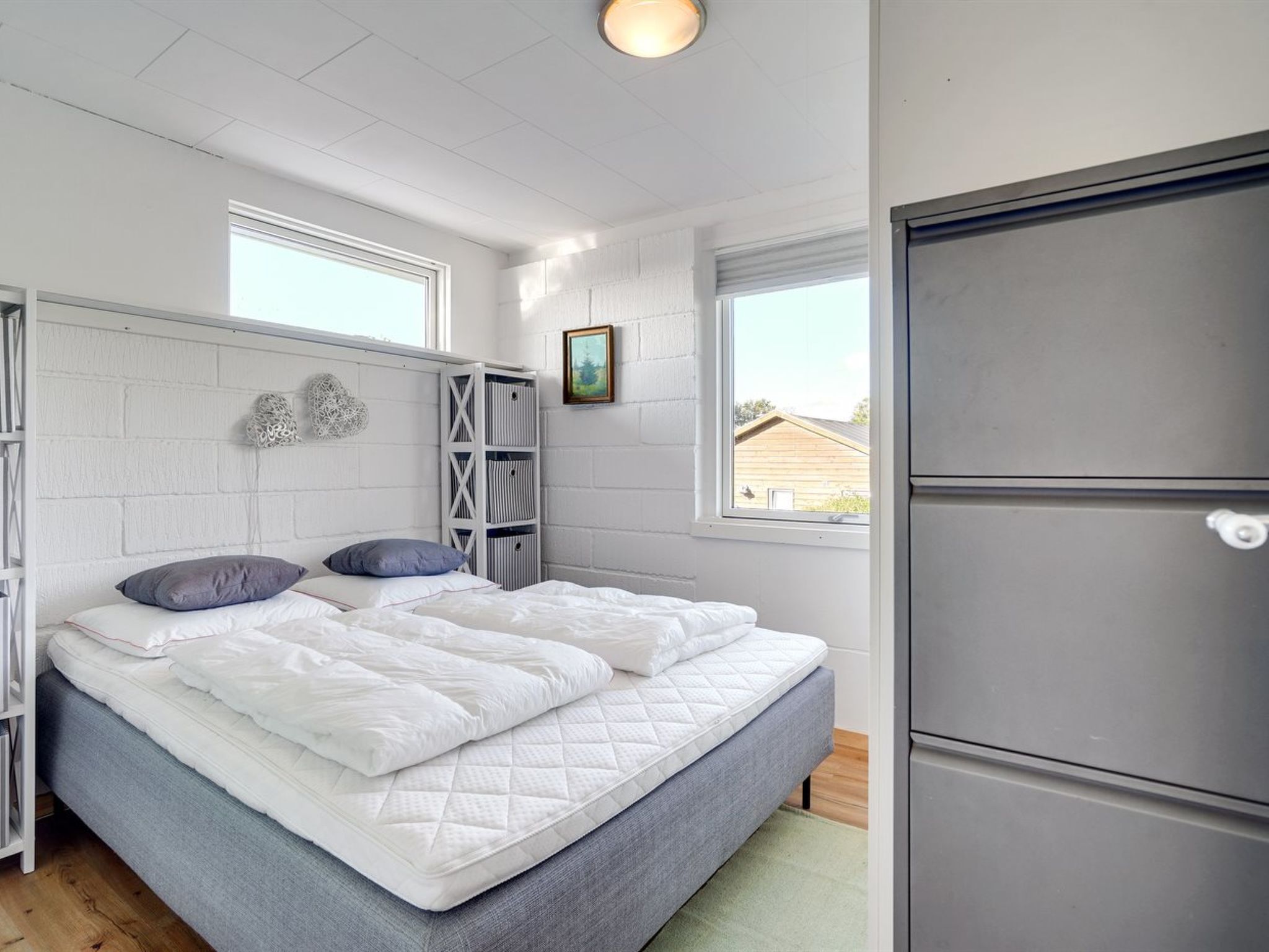 Un dormitorio con cama, paredes blancas, una ventana y un armario empotrado.