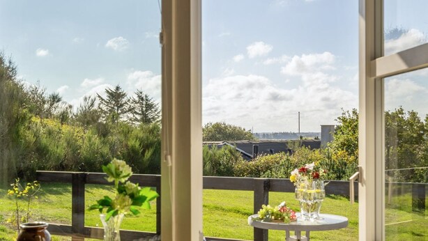 A room with a large window overlooking a grassy area and a distant view of buildings. - "Tomine" - 500m to the fjord by Interhome (Struer)