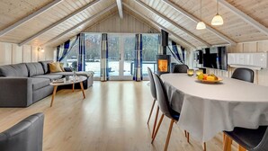 A spacious loft with a high ceiling, a cozy seating area, a dining table, and a large window offering a view of the outdoors.
