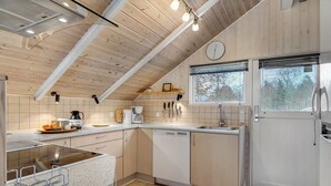 A modern kitchen with wooden ceiling beams, a built-in dishwasher, and a window with a view of trees.