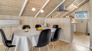 A modern kitchen with a wooden ceiling, a dining area with a table and chairs, and a view of the outdoors through a window.