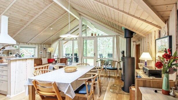 A spacious kitchen with wooden cabinets, a dining area with a table and chairs, a large window, and a wood-burning stove. - "Ellica" - 50km from the sea by Interhome (Give)