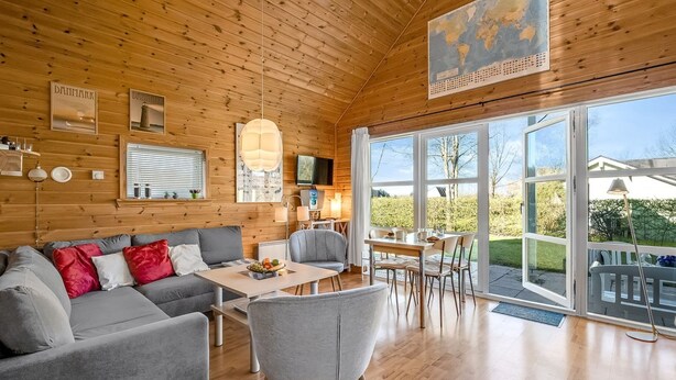 Een gezellig interieur van een chalet met houten plafond, een groot raam, een eethoek en een zithoek met een bank en stoelen.