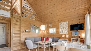 Een gezellig cabin interieur met een houten plafond, een bank, een eettafel met stoelen en een aan de muur bevestigde televisie.