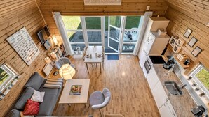 Een gezellig chalet binnen met een eethoek, keuken en een groot raam met uitzicht op een tuin.