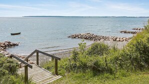 Een houten terras dat uitkomt op een rotsachtige kustlijn, met een kalm wateroppervlak en een landmassa in de verte.
