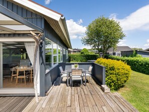 Une terrasse dotée de mobilier d’extérieur, une porte vitrée donnant sur un patio et un jardin bien entretenu.
