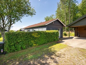 Une maison moderne avec un toit recouvert de tuiles rouges, une véranda et une haie bien entretenue.