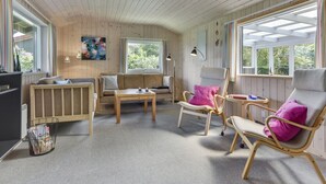 Een gezellige kamer met houten wanden en plafond, een bank, twee fauteuils, een bijzettafeltje en een vloerlamp.