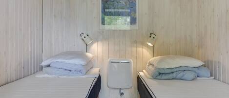 Et værelse med to senge, hver med pude og en sengebordlampe. Der er en radiator mellem sengene og et indrammet billede på væggen.