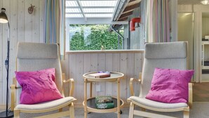 Een gezellige kamer met twee houten stoelen met kussens, een kleine tafel met een gezelschapsspel en een raam met gordijnen.