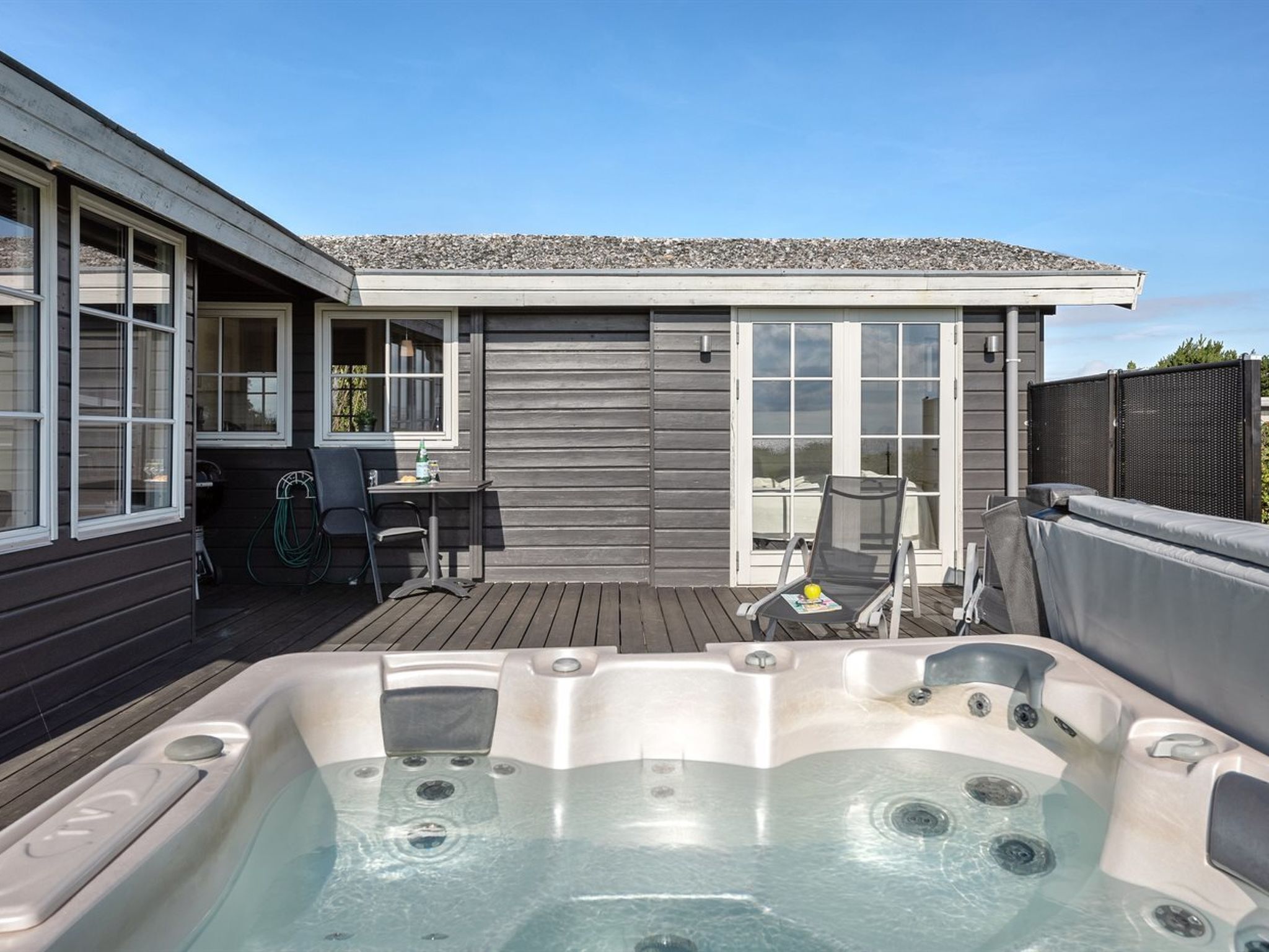 Ein Whirlpoolbereich mit Holzterrasse, einem Tisch mit Stühlen und einer überdachten Sitzgelegenheit mit Blick auf das Haus.