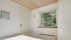 Un dormitori amb un llit, una porta, una finestra amb vista a arbres i un interruptor de llum fixat a la paret.