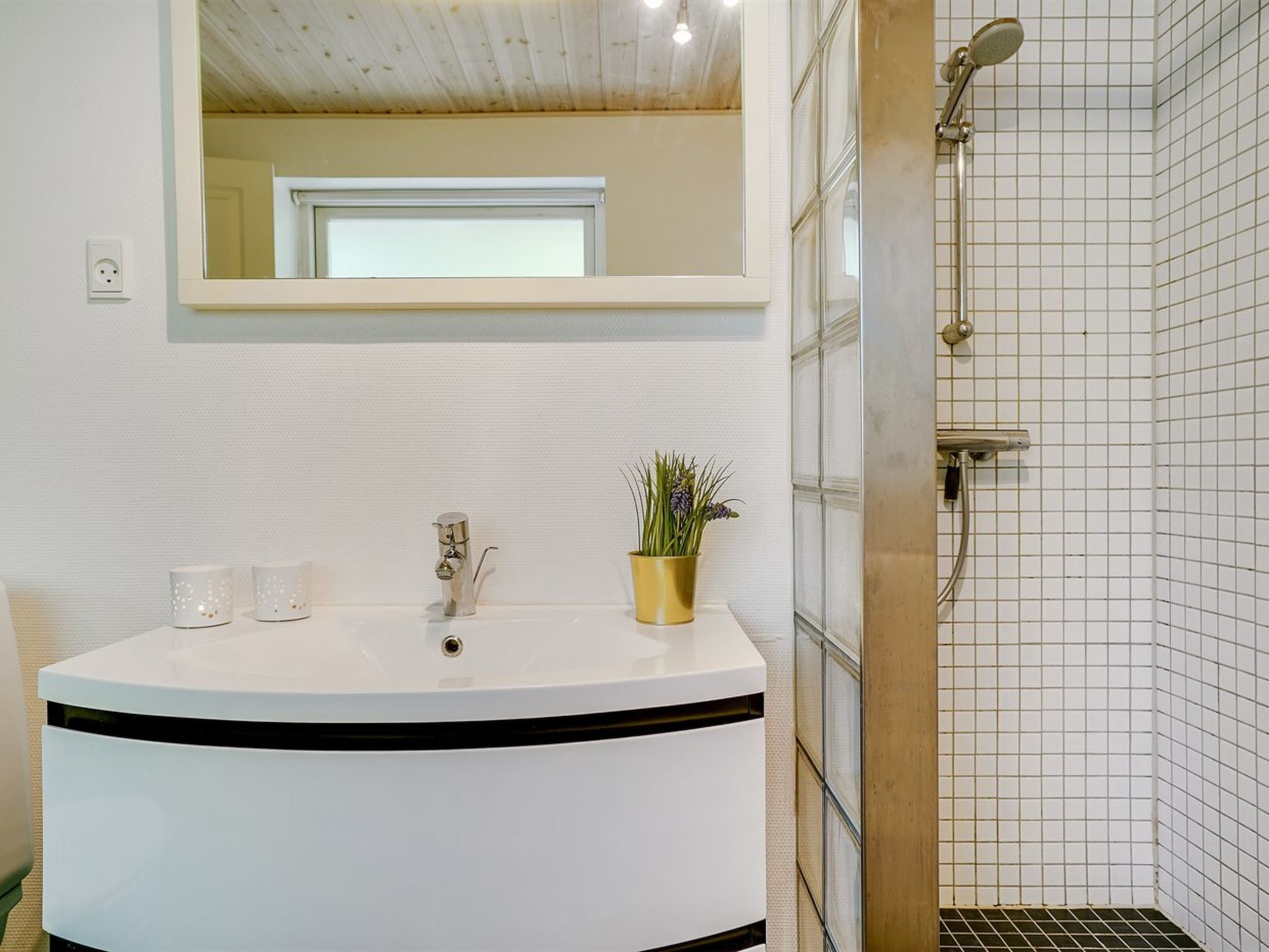 A bathroom with a white sink, a mirror above it, and a shower area with tiled walls.