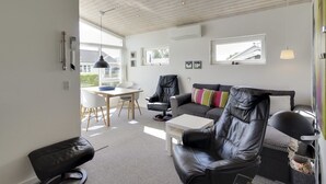 Een moderne woonkamer met een wit plafond, een zwarte leren bank, een witte eettafel met stoelen, en een zwarte lederen fauteuil.