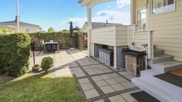 Een terras met een tafel, stoelen, een barbecue en een kleine tuin.
