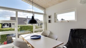 Een moderne eetruimte met een tafel, stoelen en een zwart hanglamp. Grote ramen bieden uitzicht op een woning en groen.