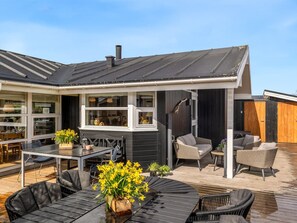 Une maison moderne dotée d’une terrasse, d’un espace salon extérieur et d’une grande fenêtre donnant sur la terrasse.