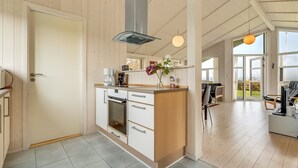 A modern kitchen with white cabinetry, a built-in oven, and a coffee maker. There is a large window providing natural light and a view of the outdoors.
