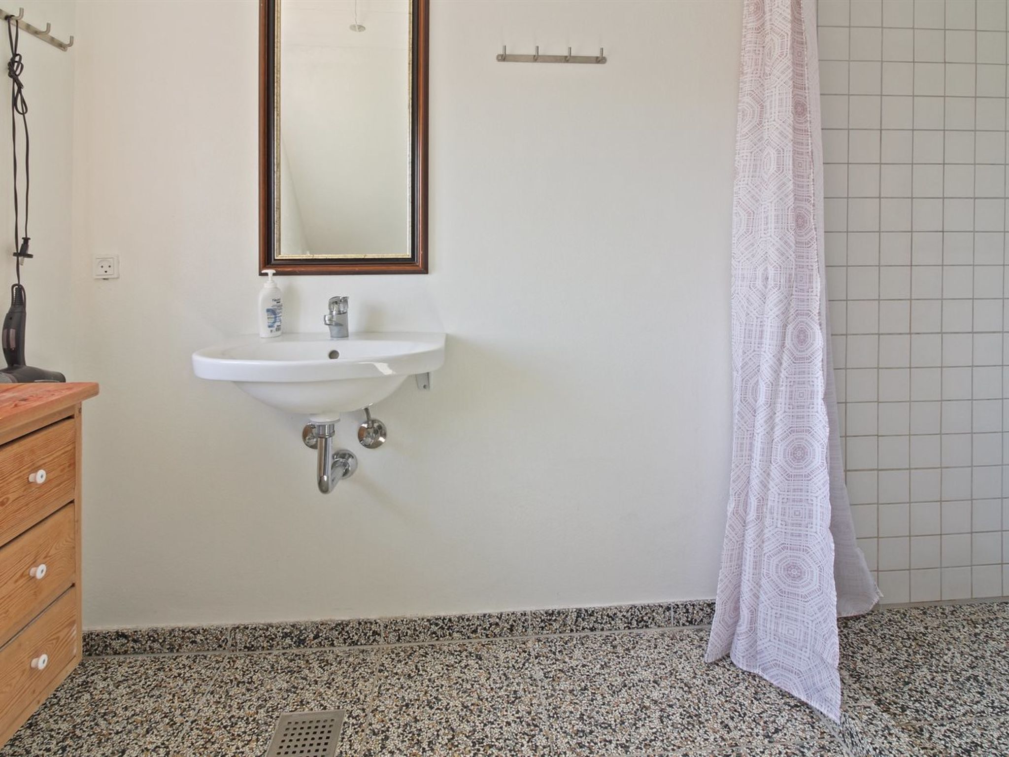 A bathroom with a white sink, wooden cabinet, and patterned shower curtain.