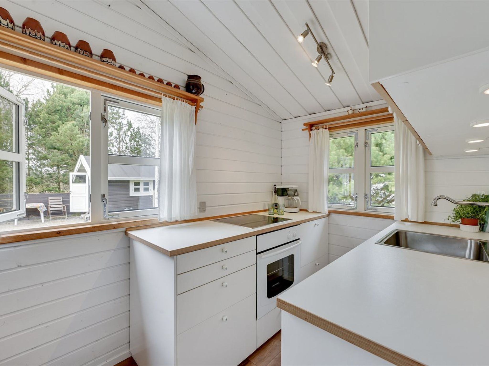 A modern kitchen with white cabinetry, wooden countertops, and a built-in oven. There are large windows providing natural light and views of the surrounding area.
