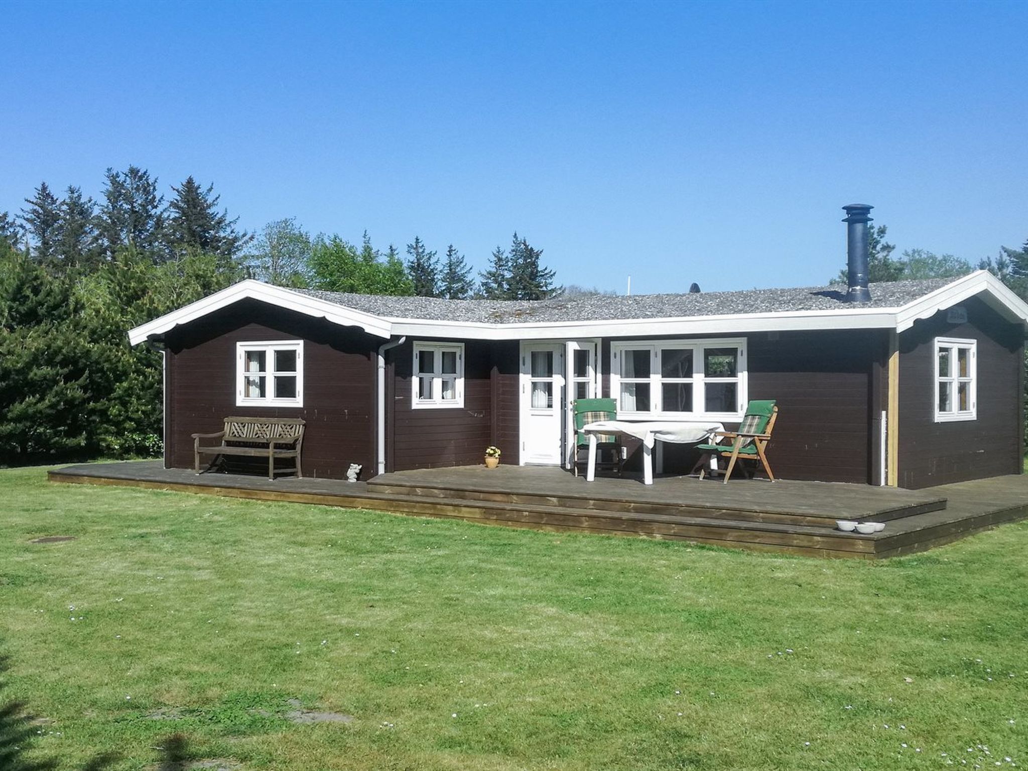A brown wooden building with a porch, a table, and chairs.