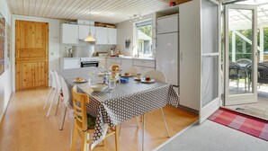 A compact kitchen with white cabinets, a dining table with a patterned tablecloth, and a wooden door. - "Ulrike" - 600m to the fjord by Interhome (Ulfborg)