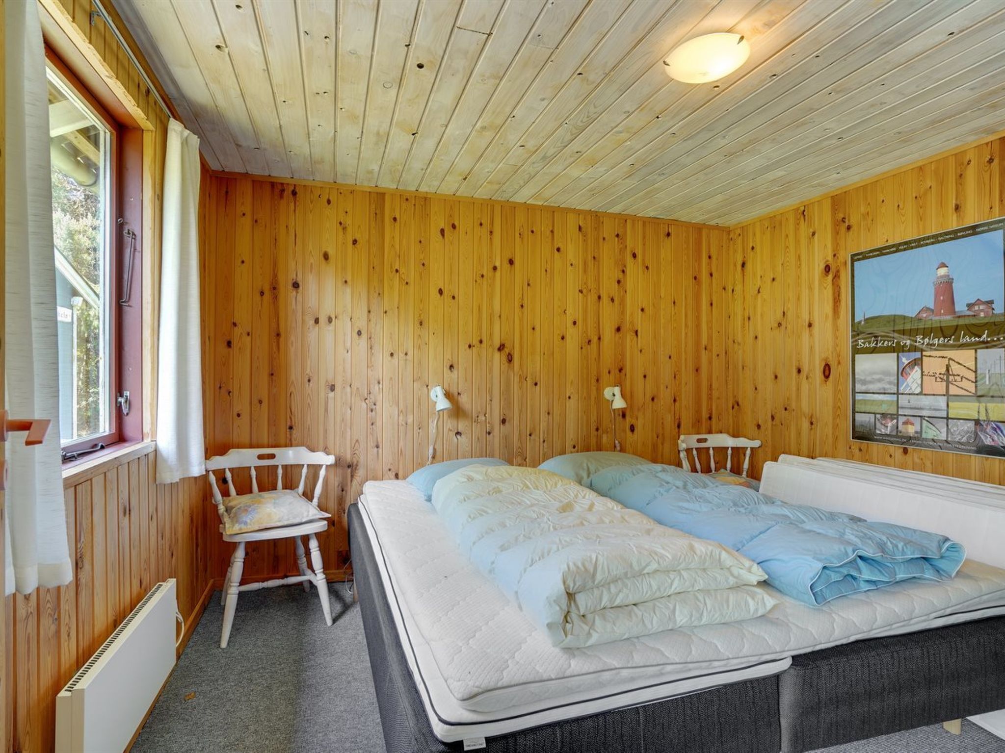 Een houten kamer met twee bedden, een raam, een radiator en een poster aan de muur.