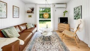 Ein Wohnzimmer mit braunem Ledersofa, einem runden Couchtisch, einem hängenden Korbstuhl und einem Fernsehschrank.