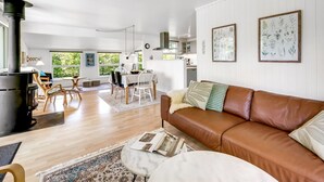Ein geräumiger Wohnbereich mit braunem Ledersofa, einem Esstisch mit Stühlen, einer Küche im Hintergrund und einem großen Fenster, das für natürliches Licht sorgt.