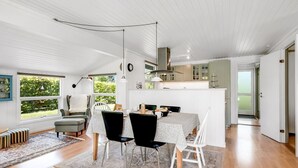 Eine moderne Küche mit weißen Schränken, ein Essbereich mit Tisch und Stühlen sowie eine gemütliche Sitzecke mit Sofa und Teppich.