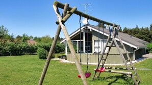 En gungställning i trä på en gräsplätt, med ett hus i bakgrunden.