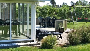 En uteplats med ett takförsett sittområde, utemöbler och en trädgård.