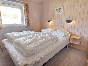 Una cama individual con ropa blanca en una habitación con paredes de madera y una ventana con cortinas.