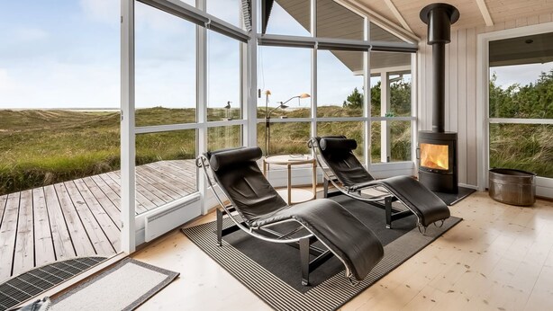 A modern interior with large windows, a wood-burning stove, and two lounge chairs on a wooden deck. - "Leona" - 250m to the fjord by Interhome (Ulfborg)