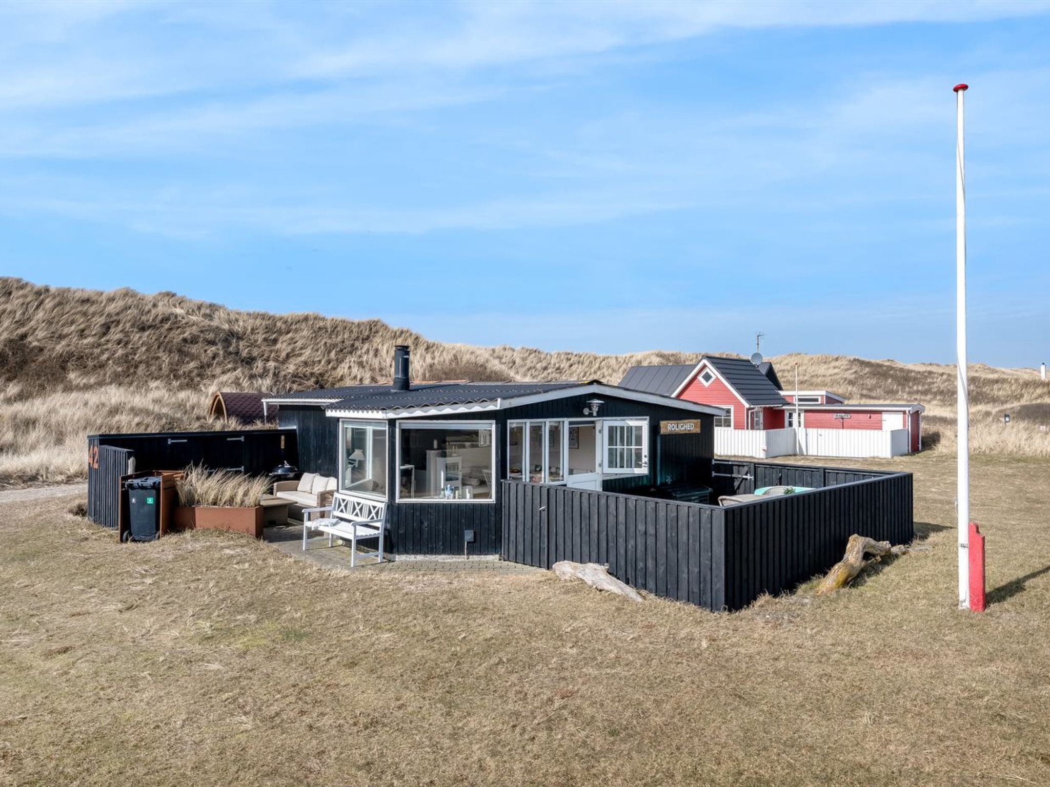 Un bâtiment situé sur la côte, avec une façade noire, une structure rouge et blanche en arrière-plan et un mât de drapeau.