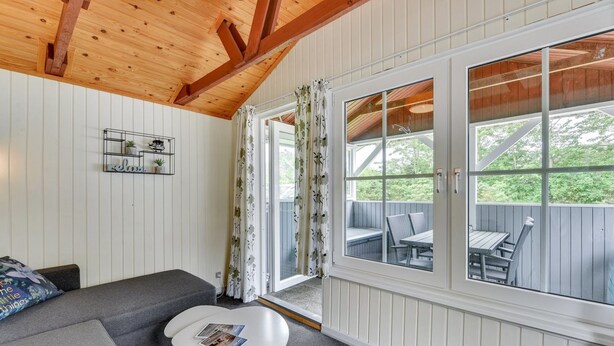 A cozy room with a wooden ceiling, a gray sofa, a small white table, and a window with a view of outdoor furniture. - "Elizabeth" - 400m to the fjord by Interhome (Ulfborg)