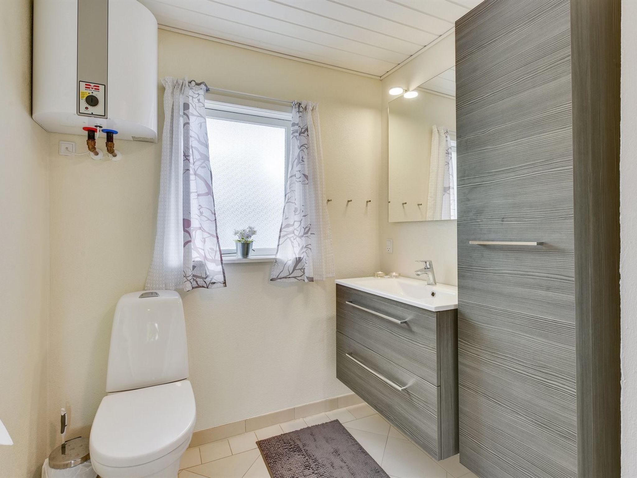 A bathroom with a toilet, a sink, a mirror, and a window with curtains.