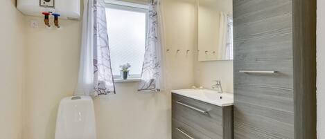 A bathroom with a toilet, a sink, a mirror, and a window with curtains.