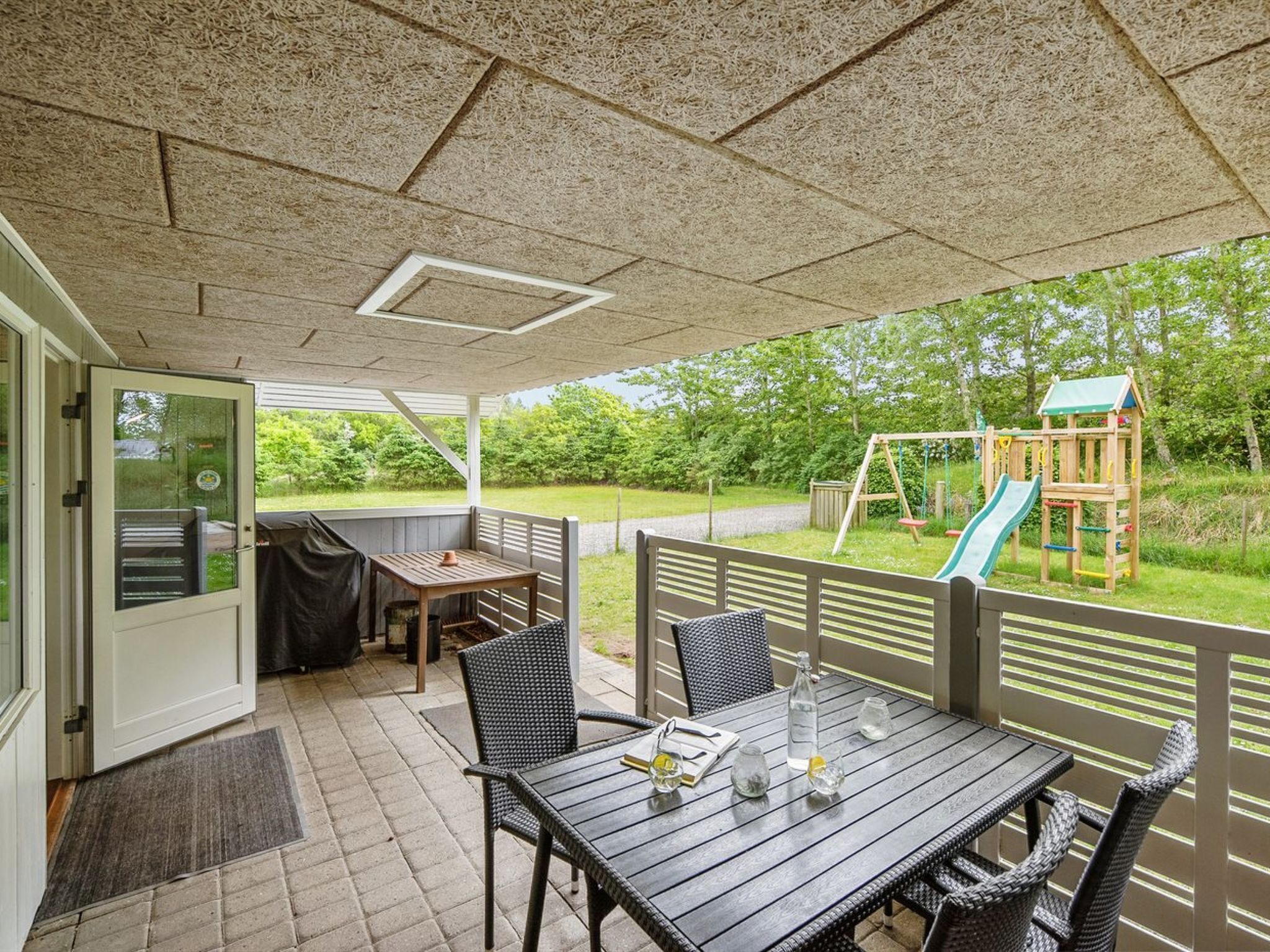 A covered patio area with a table and chairs, a play structure in the background, and a door leading to the interior.