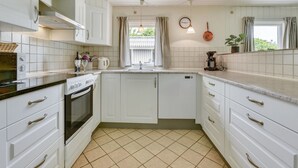 A compact kitchen with white cabinets, a tiled floor, a sink, a stove, and a clock on the wall. - "Elizabeth" - 400m to the fjord by Interhome (Ulfborg)