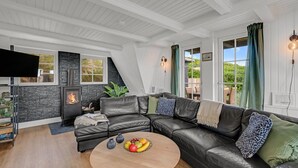 Una sala de estar moderna con un sofá de cuero negro, una mesa redonda de madera con fruta, una chimenea de piedra y un televisor montado en la pared.
